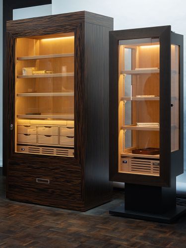 Cigar cabinets made of fine woods with glass doors and warm interior lighting.