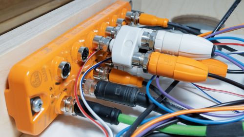 Orange IO-Link module to whose sockets various cables are connected using M12 connectors